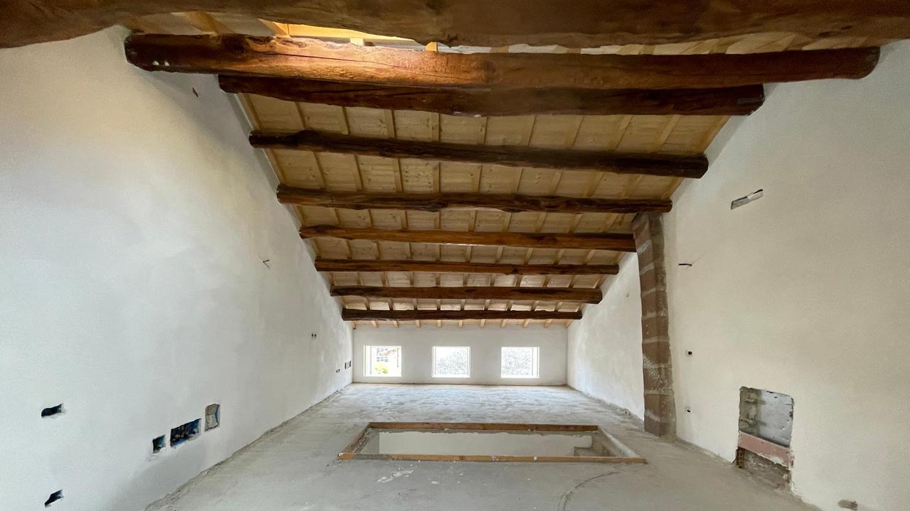 Interno vuoto di una casa in ristrutturazione con pareti bianche e soffitto con travi in legno